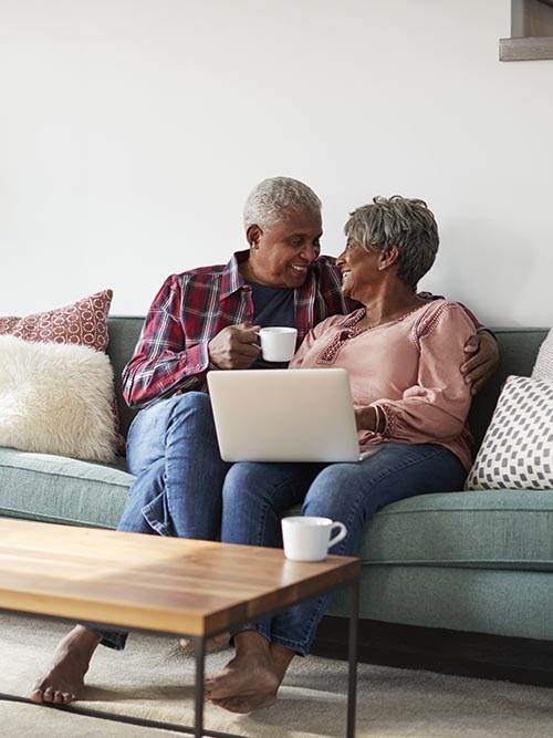 smiling retired man and woman sitting on their couch drinking coffee and sharing a laptop